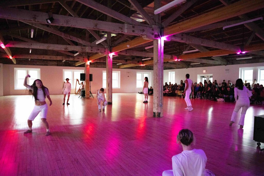 performers in white dancing in a pink woom with people watching