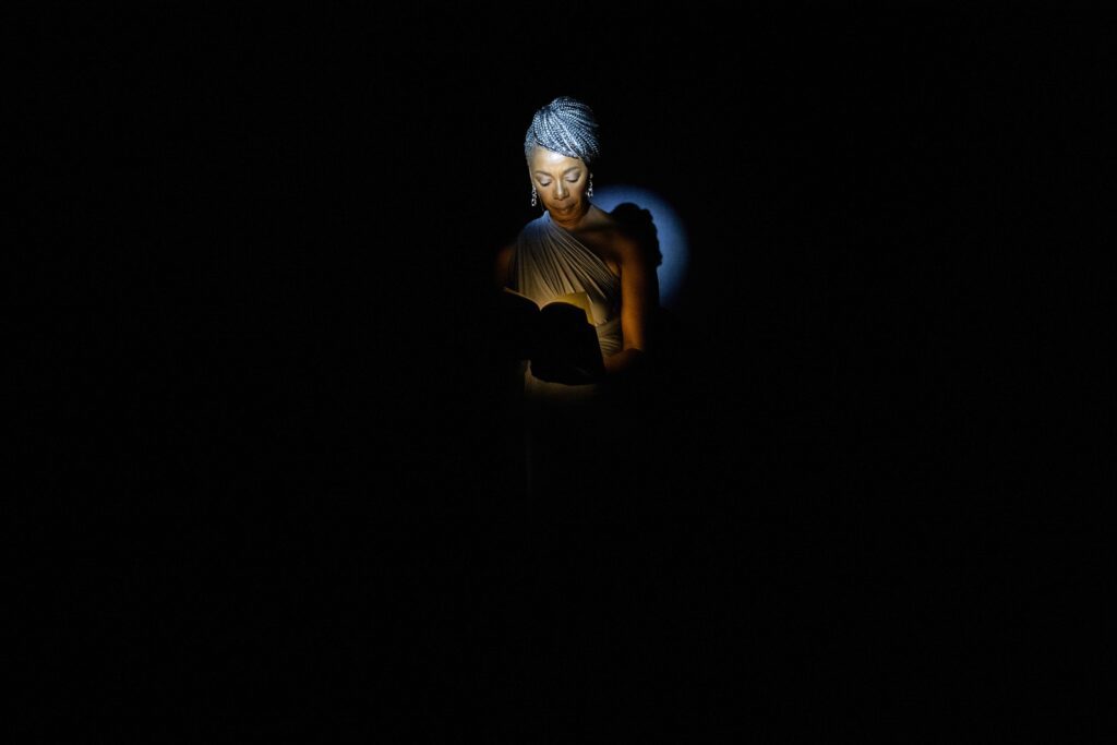 performer reading in focal light in a somber space