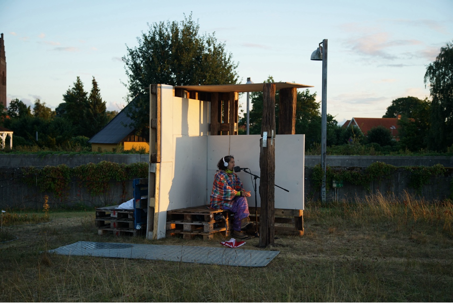 person with headphones and a microphone in a wooden construction, alone. Økocity 2.0